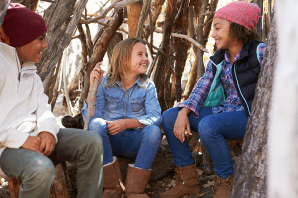 Three children sitting in a woodland den they’ve built