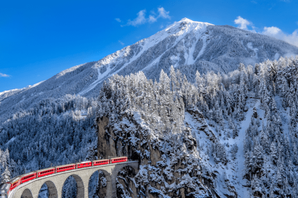 The Glacier Express in Switzerland passing over a viaduct in a snowy, mountainous landscape