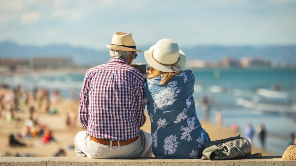 An older couple sitting on a wall at a beach
