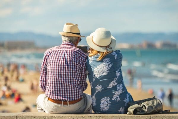 An older couple sitting on a wall at a beach