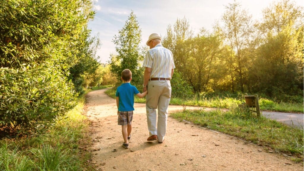 A grandfather and grandchild walking through a park